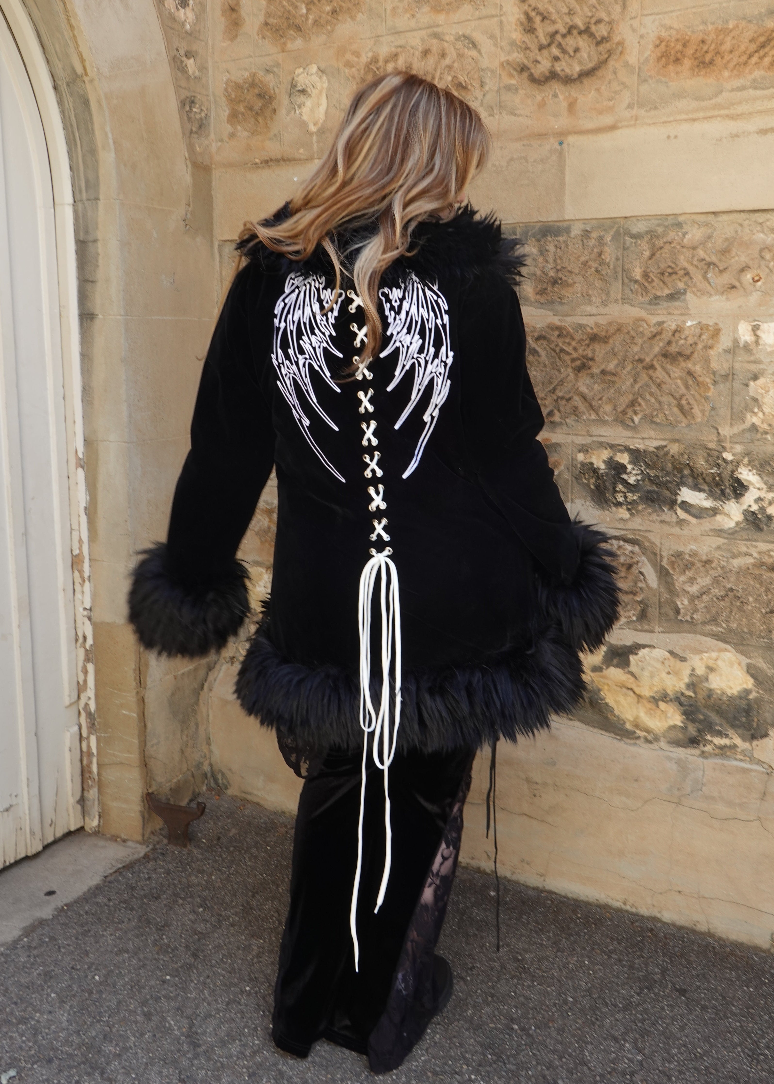 Back view of black velvet coat with fur trim showcasing bold embroidered white angel wings and cross-stitch design. On model - Raven's Embrace - FM2U Clothing Australia | Gothic Alternative Whimsical Ethical Fashion